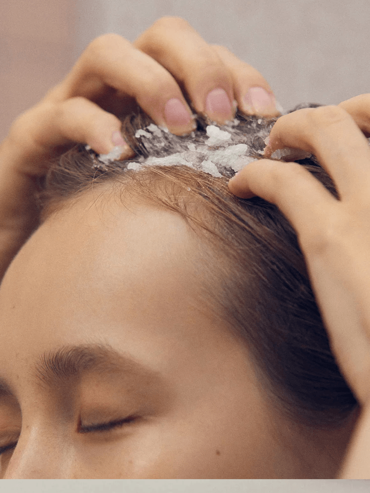 Woman applying AROMATICA Rosemary Scalp Scrub with Andes lake salt to her scalp for deep exfoliation.