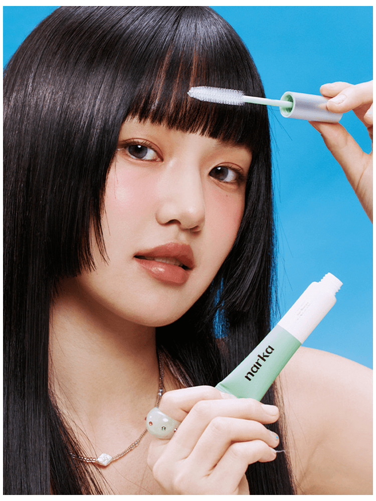 Model holding NARKA Fresh Sebum Hair Mascara 15g with a blue background, showcasing glossy hair application.