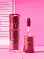 romand The juicy lasting tint Mini 1g product image showcasing a glossy lipstick and wand on a vibrant pink background.