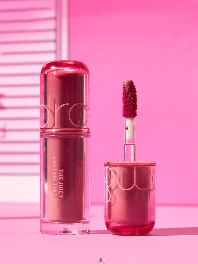 romand The juicy lasting tint Mini 1g product image showcasing a glossy lipstick and wand on a vibrant pink background.