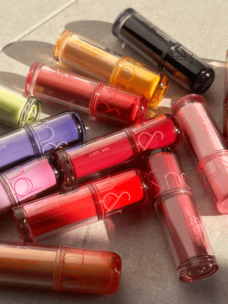 rom&nd The juicy lasting tint Mini 1g lip tint collection in various vibrant colors arranged artfully.