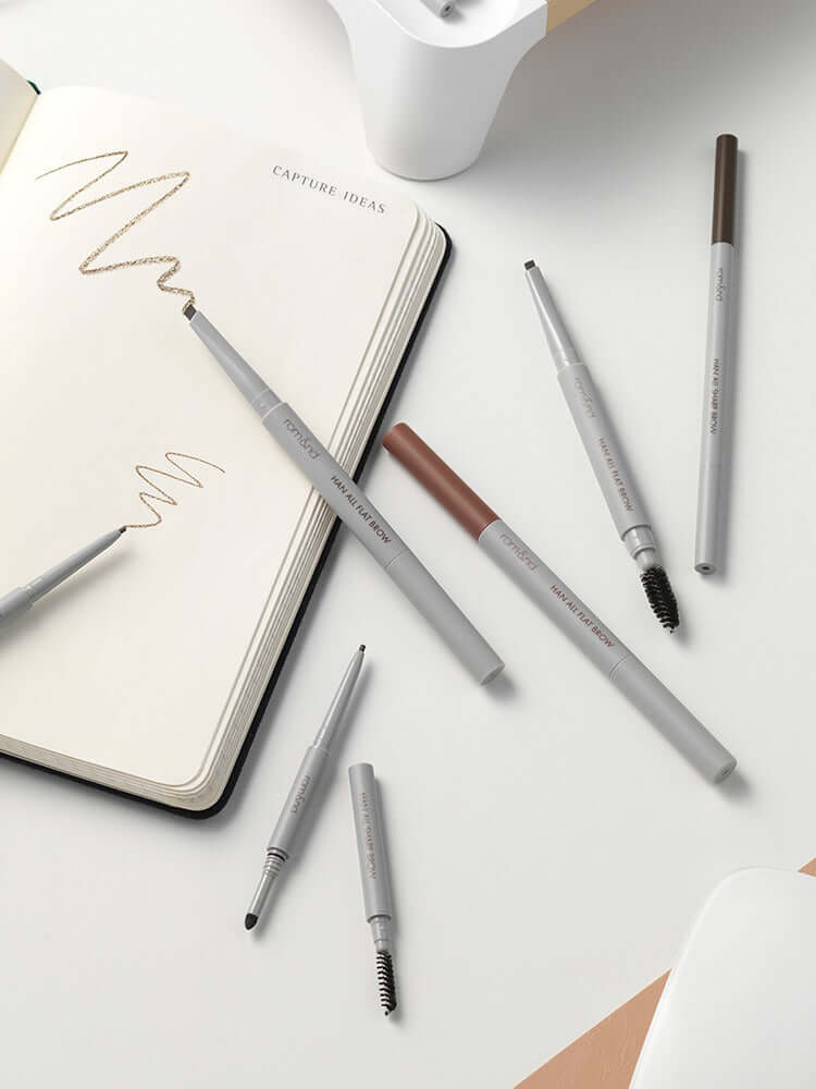 rom&nd Han All Flat / Sharp Brow makeup pencils arranged around a notebook for natural brow definition.