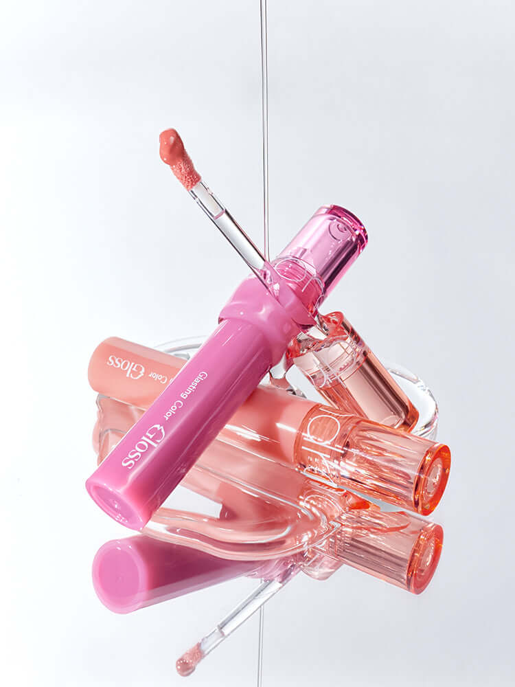 rom&nd Glasting Color Gloss 4g in a stylish arrangement with pink and clear gloss tubes on a reflective surface.