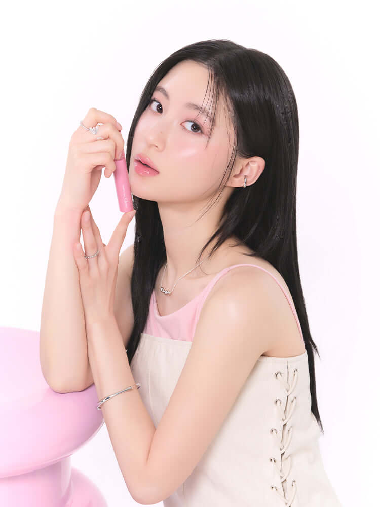 rom&nd Glasting Color Gloss 4g model holding the product with a soft pink background and hairstyle.