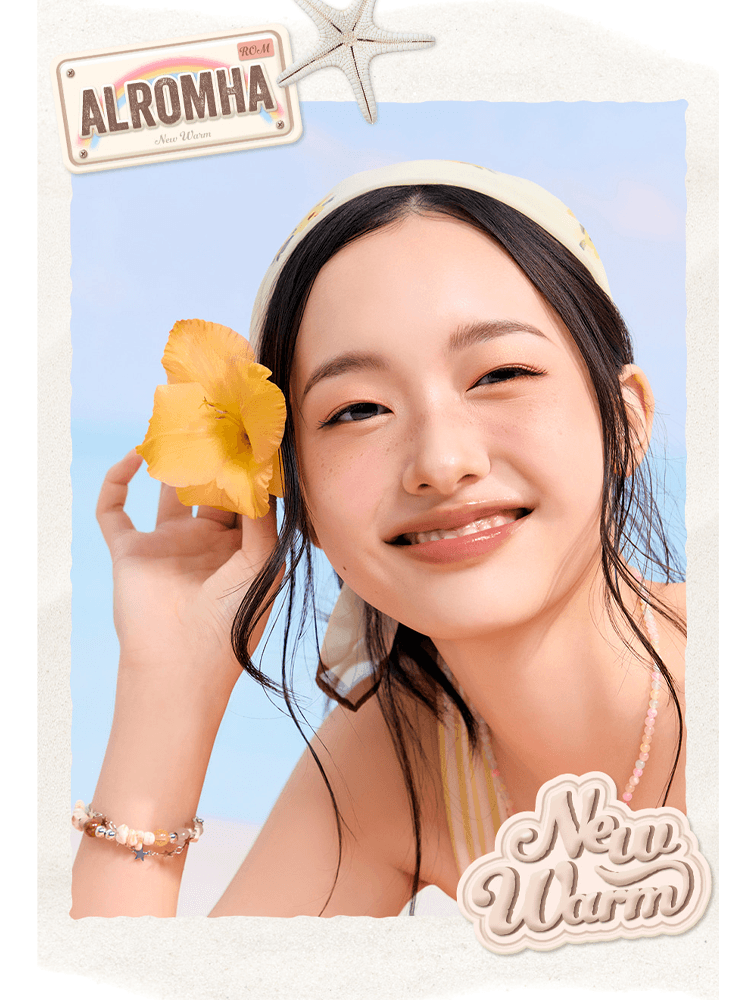 A smiling woman with a flower in her hair showcasing romnd The Juicy Lasting Tint NEW WARM in a bright beach setting.