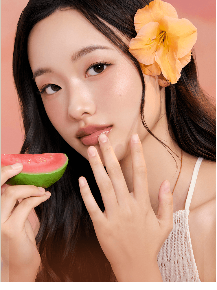 Model showcasing romnd The Juicy Lasting Tint NEW WARM, holding a watermelon slice with a floral accent in her hair.
